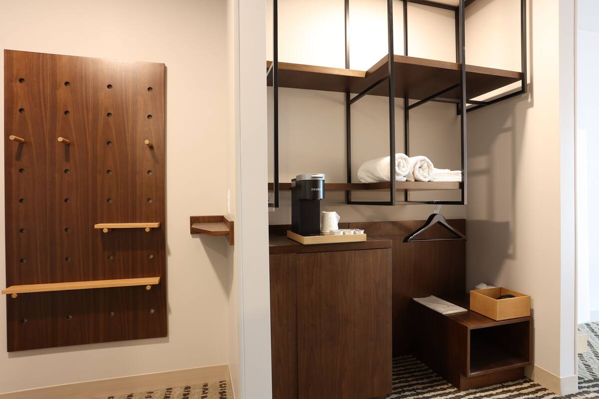 A modern bathroom with a wooden vanity, a towel rack, a coffee maker, and a small wooden box.