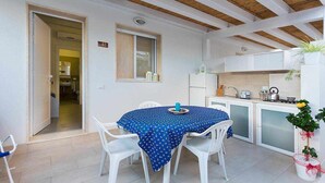 A small, open-plan kitchen and dining area with white cabinets, a blue tablecloth-covered table, and white chairs. - (MP62) Modern studios with veranda 150 mt from the sea (Marina di Modica)