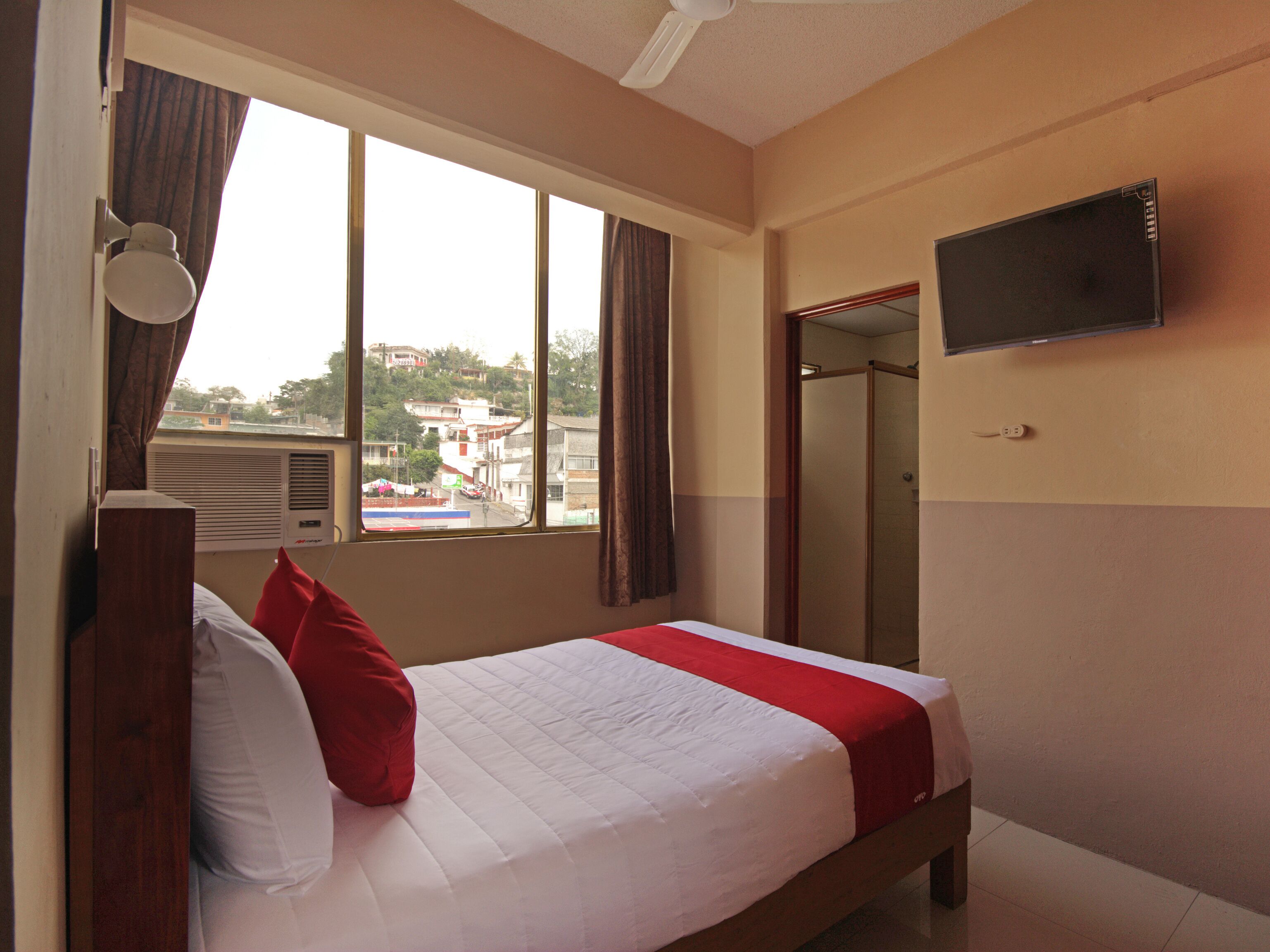 A hotel room with a bed, a TV mounted on the wall, a window with curtains, and a view of the outside.