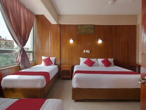 A hotel room with two beds, wooden paneling, a painting on the wall, and a window with curtains.