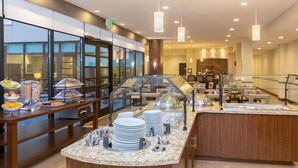 Un espace buffet proposant divers plats, une vitrine réfrigérée et un coin salon à l’arrière-plan.