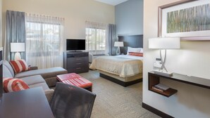 Une chambre d’hôtel avec un lit, un canapé, un bureau, une télévision et un tableau au mur.