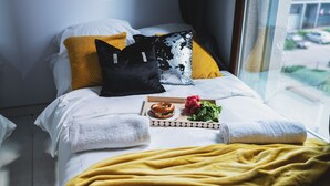 A neatly made bed with white linens, a yellow throw blanket, and a breakfast tray with a sandwich, radishes, and greens. - P&O Kolejowa 3 (Warsaw)