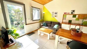 Un salon moderne avec un canapé, une table basse et une table à manger. Une fenêtre offre une vue sur la verdure à l’extérieur.