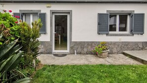 Une maison de plain-pied avec un toit en tuiles, une cheminée, une porte d’entrée et un petit jardin agrémenté de plantes en pot.