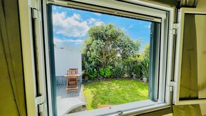 Une fenêtre donnant sur un jardin, une chaise en bois et un mur blanc.