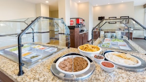 Zona de bufé con diversas opciones de comida, incluyendo un plato de carne, papas fritas y tortillas.