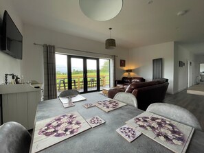 A modern living room with a dining area, large sliding glass doors to a deck, and a flat-screen TV mounted on the wall.