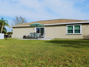 A single-story house with a patio area featuring a table and chairs, a green umbrella, and a white fence.