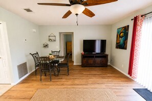 A living room with a dining table, chairs, a ceiling fan, a television on a wooden stand, and a painting on the wall. - ~~Coastal Den of Zen by Megan~~ (Port St. Lucie)