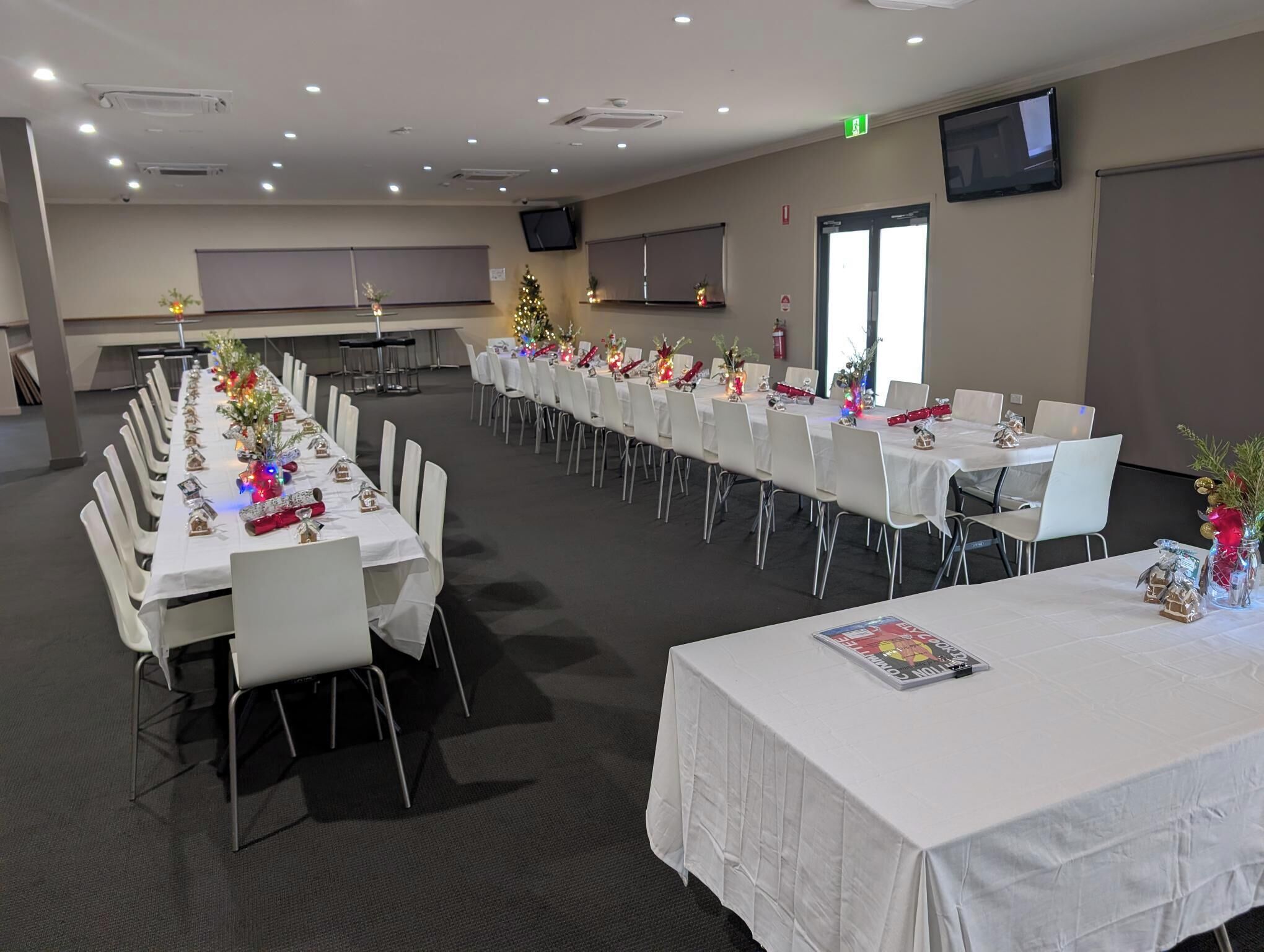 A conference room with long tables, white chairs, and Christmas decorations.
