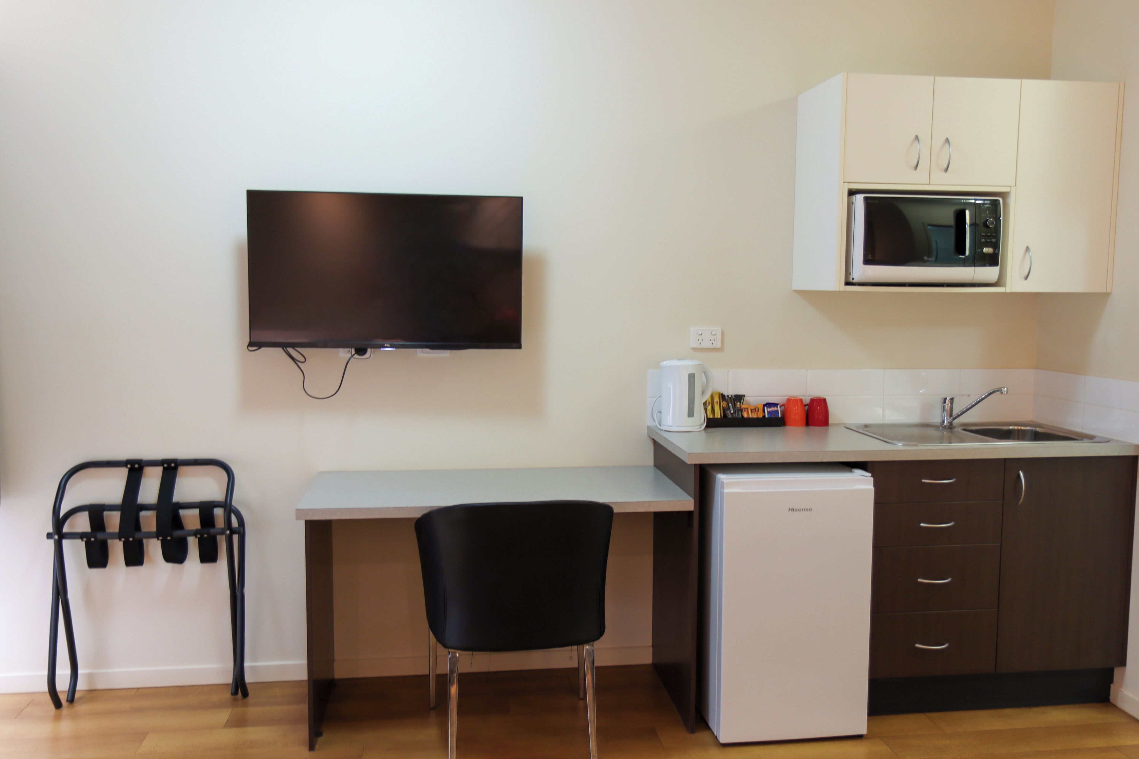 A compact kitchenette with a microwave, sink, and a small refrigerator. A flat-screen TV is mounted on the wall above the counter.