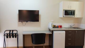 A compact kitchenette with a microwave, sink, and a small refrigerator. A flat-screen TV is mounted on the wall above the counter.