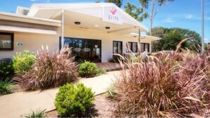 A modern building with a covered entrance, surrounded by landscaped gardens. - Weipa Motel Resort (Rocky Point)