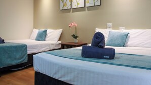 A hotel room with two beds, a small table, a vase with flowers, and artwork on the wall. - Weipa Motel Resort (Rocky Point)