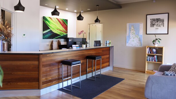 A modern kitchen with a wooden island, bar stools, pendant lighting, and a bookshelf. - Weipa Motel Resort (Rocky Point)