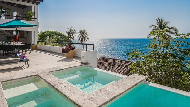 Zona de piscina con vista al océano, comedor con mobiliario exterior y una escalera que lleva a un nivel superior.