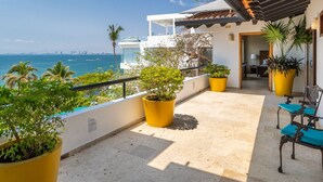 Un balcón con plantas en macetas, vistas al mar y una zona de estar con sillas.