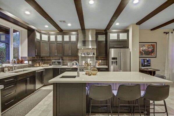 A modern kitchen with dark cabinets, stainless steel appliances, and a large island with bar stools.