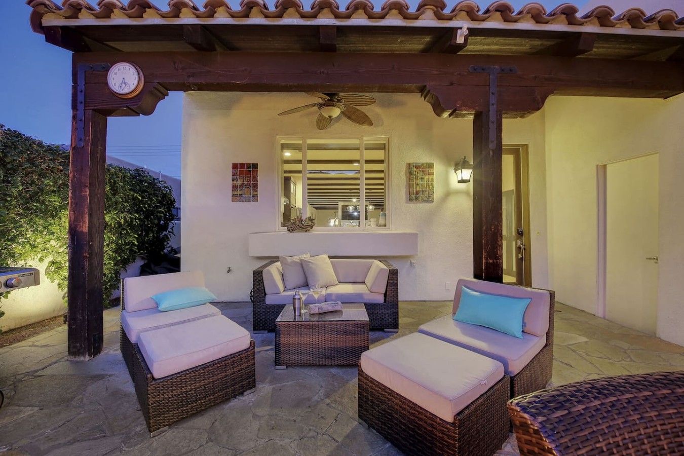 An outdoor patio area with wicker furniture, a ceiling fan, and a clock on a post.