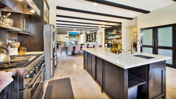 Een moderne keuken met roestvrijstalen apparatuur, een groot eiland met een spoelbak, en een eetgedeelte op de achtergrond.