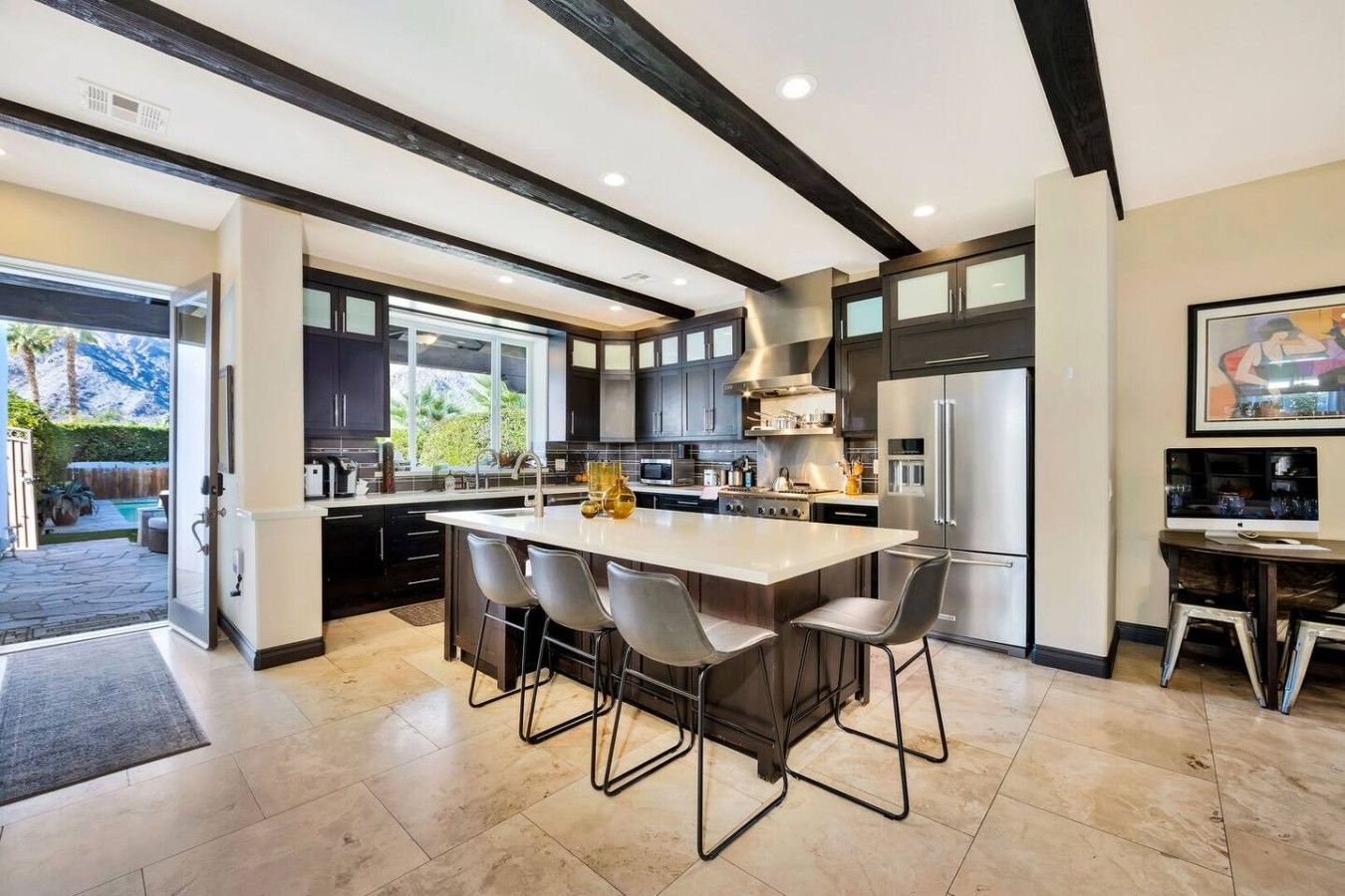 A modern kitchen with a central island, dark cabinetry, and a large window.