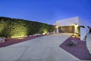 A modern house with a garage, a well-maintained hedge, and a gravel driveway.