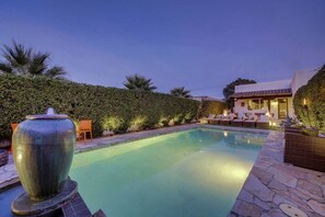 Una piscina con una fuente, rodeada de setos y mobiliario de exterior.