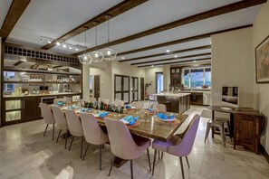 Un comedor amplio con una larga mesa dispuesta para una comida, flanqueada por sillas modernas, y una zona de cocina con una isla grande y electrodomésticos integrados.