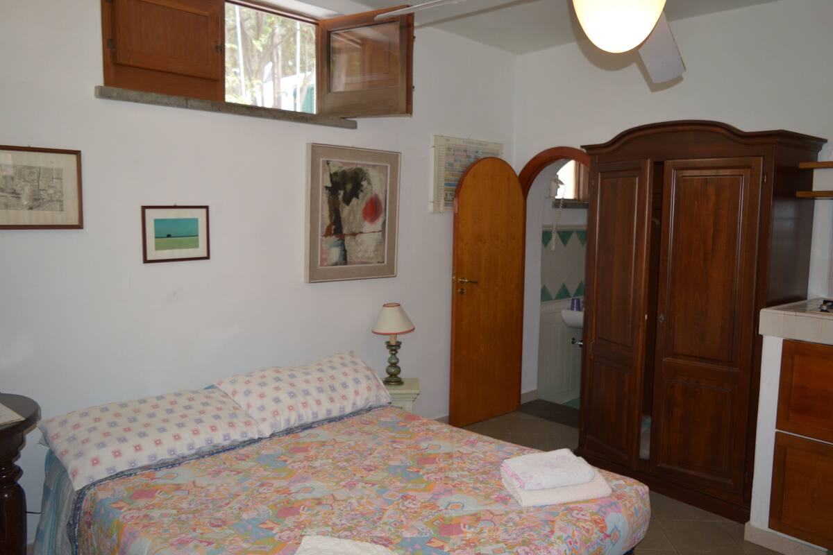 A bedroom with a bed, a wooden wardrobe, a nightstand with a lamp, and framed pictures on the wall.