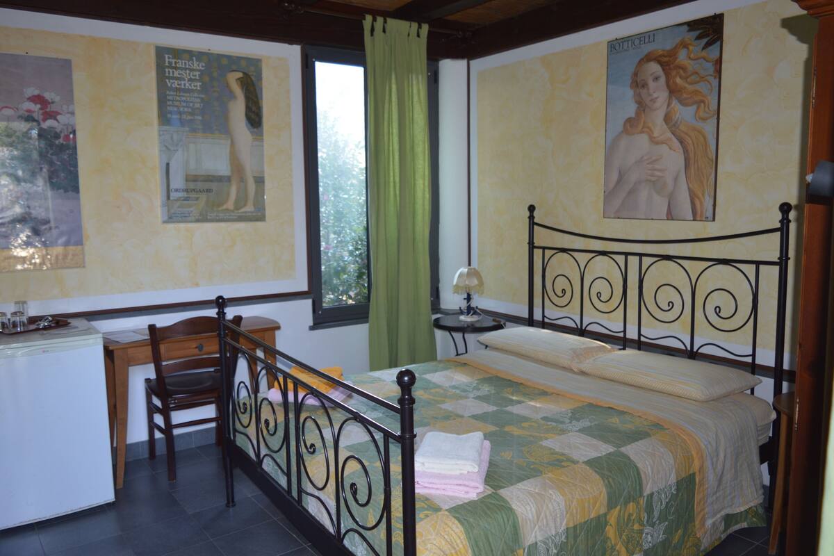 A bedroom with a bed, a desk, a chair, and a window with curtains.