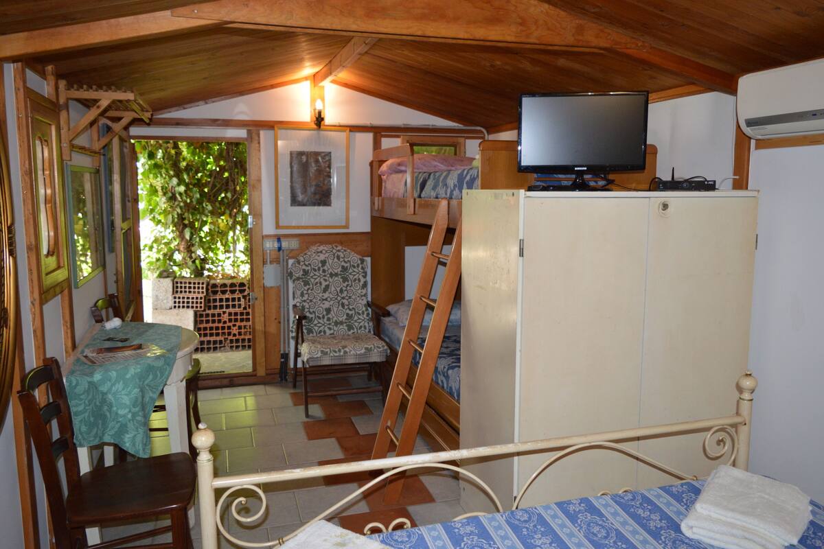 A compact room with a bunk bed, a television on a cabinet, a dining table with chairs, and a patterned chair.