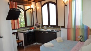 Un angolo cottura funzionale con piano cottura, lavello e pensili, una piccola zona pranzo con una sedia e un letto con copriletto blu.