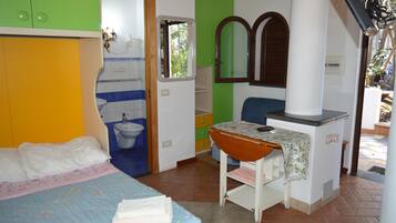 A bedroom with a bed, a small table, a mirror, and a bathroom with a toilet and sink.
