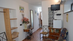 Un accogliente soggiorno con una poltrona in legno, un tavolino con un vaso di fiori, un televisore a parete e una libreria.