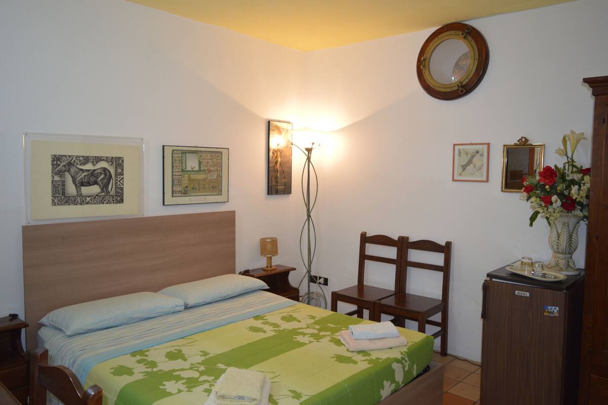 A bedroom with a bed, a chair, a desk, a mirror, and artwork on the walls.