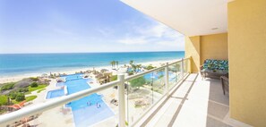 A balcony with a view of a beach resort, including a pool area and a sandy beach.