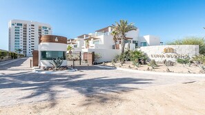 A modern building with a gated entrance, a sign reading "LUNABLANCA," and a desert landscape with sparse vegetation.