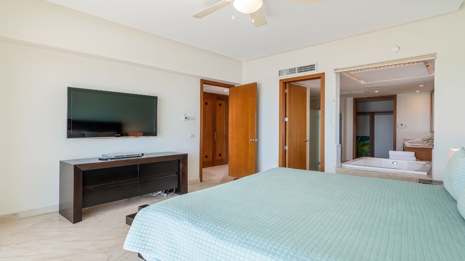 Una camera da letto con un letto grande, una TV fissata al muro, un comodino in legno scuro e un bagno con vasca e doccia.