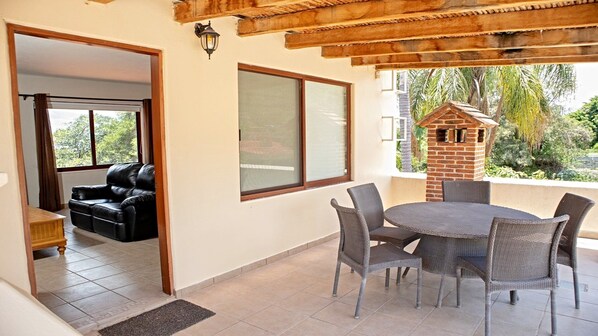 A covered patio area with a dining table and chairs, a leather sofa, and a brick-built structure.