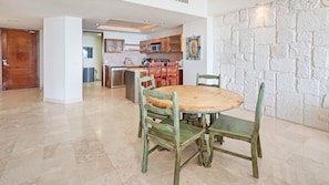 A spacious kitchen with modern appliances, a dining area with a wooden table and green chairs, and a stone accent wall.