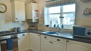 A kitchen with white cabinets, a stove, a sink, and a microwave. - 2 bedroom accommodation in Beadnell, near Alnwick (Beadnell, near Alnwick)