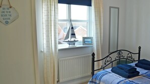 A bedroom with a bed, a window with curtains, a radiator, and a small sailboat model on the windowsill. - 2 bedroom accommodation in Beadnell, near Alnwick (Beadnell, near Alnwick)