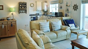 A cozy living room with a sofa, a wooden cabinet, and a dining table. - 2 bedroom accommodation in Beadnell, near Alnwick (Beadnell, near Alnwick)