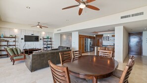 A spacious living area with a large round wooden table, multiple chairs, a built-in kitchen, and a stone accent wall.