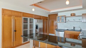 A modern kitchen with wooden cabinets, a stainless steel refrigerator, a dishwasher, and a granite countertop.