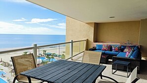 Un balcón con vistas a la playa y al océano, un sofá con cojines de colores, y una mesa.