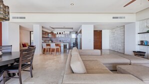 A spacious living area with a large sofa, a dining table with chairs, and a kitchen in the background.