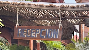 Un letrero de madera con la palabra 'RECEPTION' escrita, colgado debajo de una estructura de techo de paja.