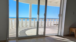 A room with a sliding glass door leading to a balcony with a white balustrade and a view of the beach. - Fully Remodeled, The Suite at Rocky Point 2 Ocean front (Puerto Penasco)